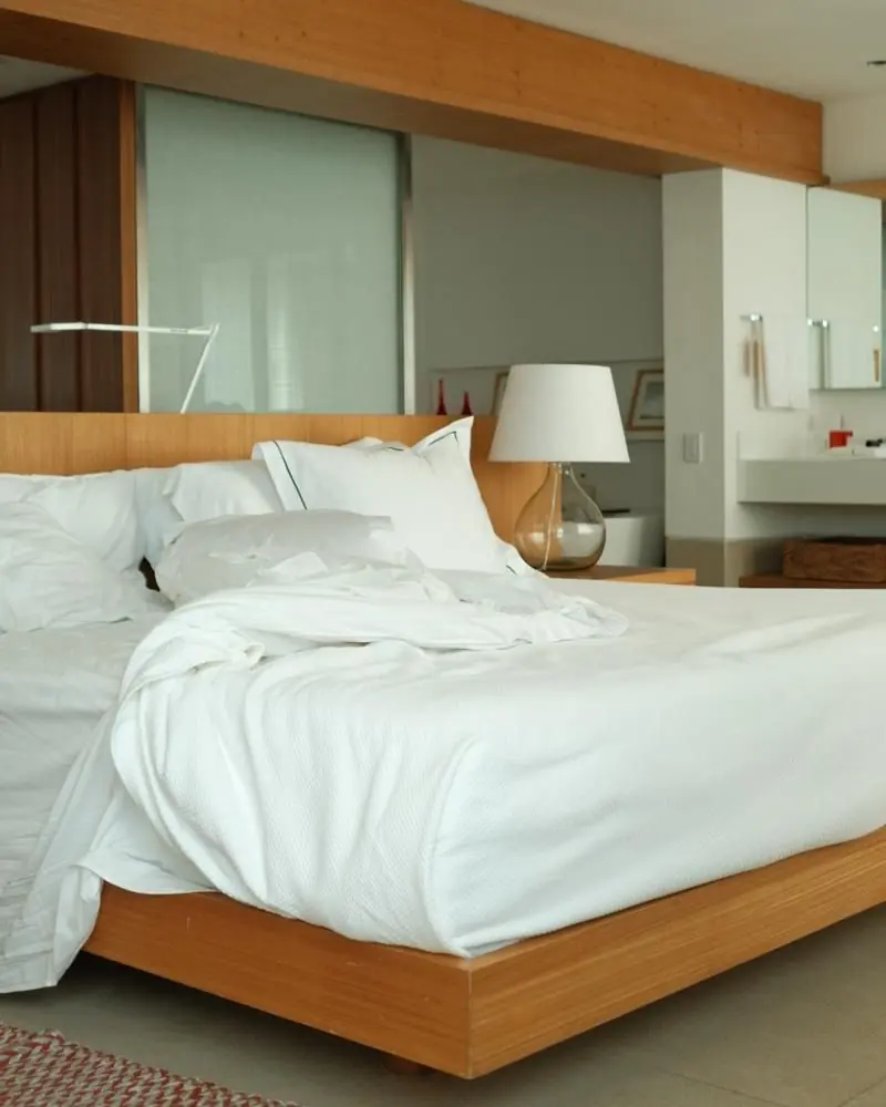 A white bed on a low wooden frame in a bright guest room