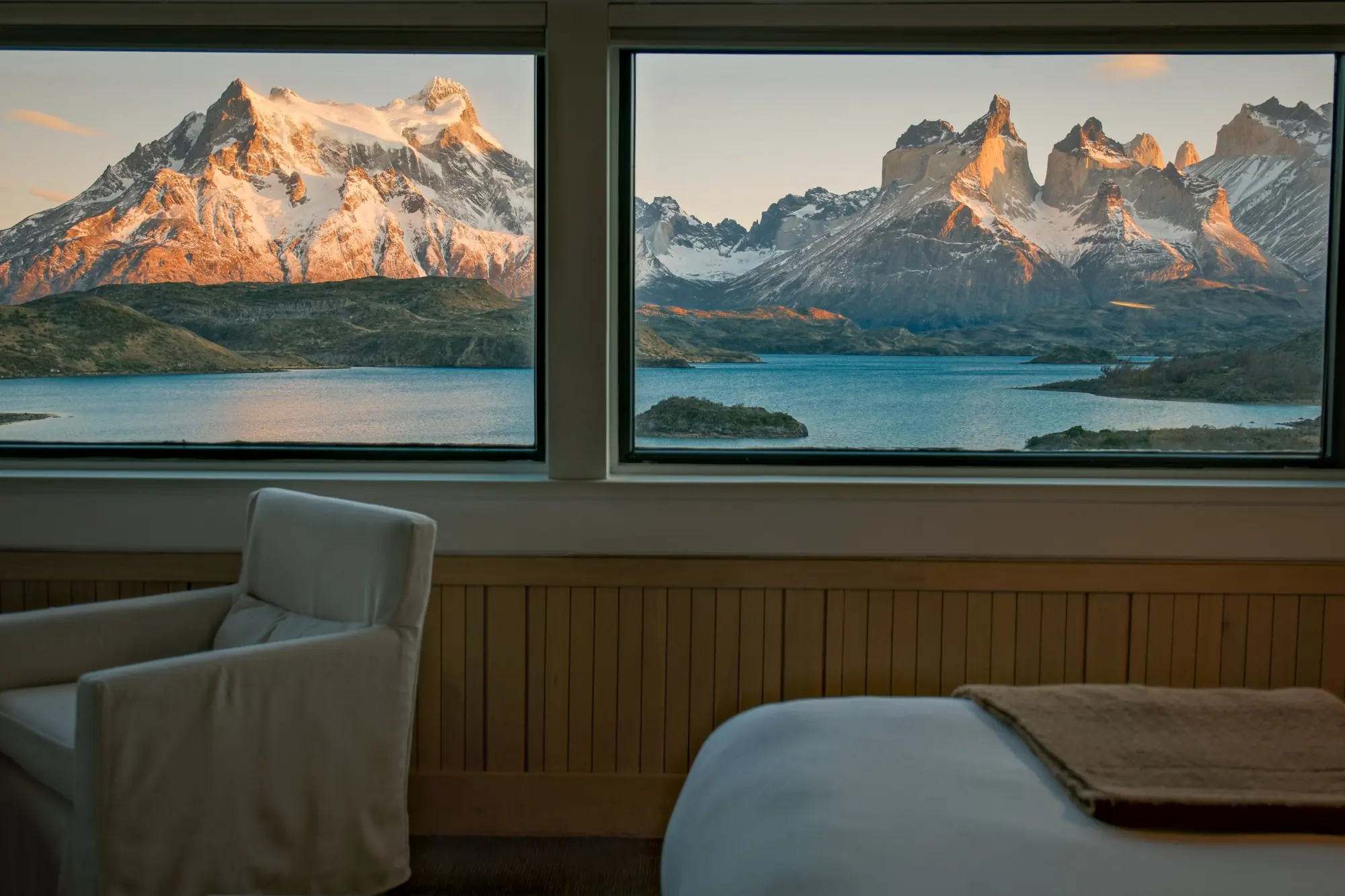 Explora Patagonia’s lit windows at dusk, with alpenglow on Paine Grande and the Cuernos del Paine behind